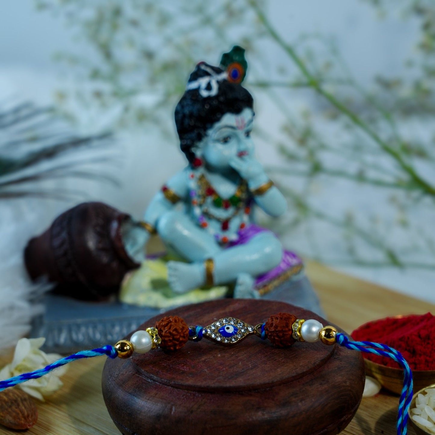Blue Evil Eye Rakhi with Rudraksha beads placed near Krishna idol for Raksha Bandhan.