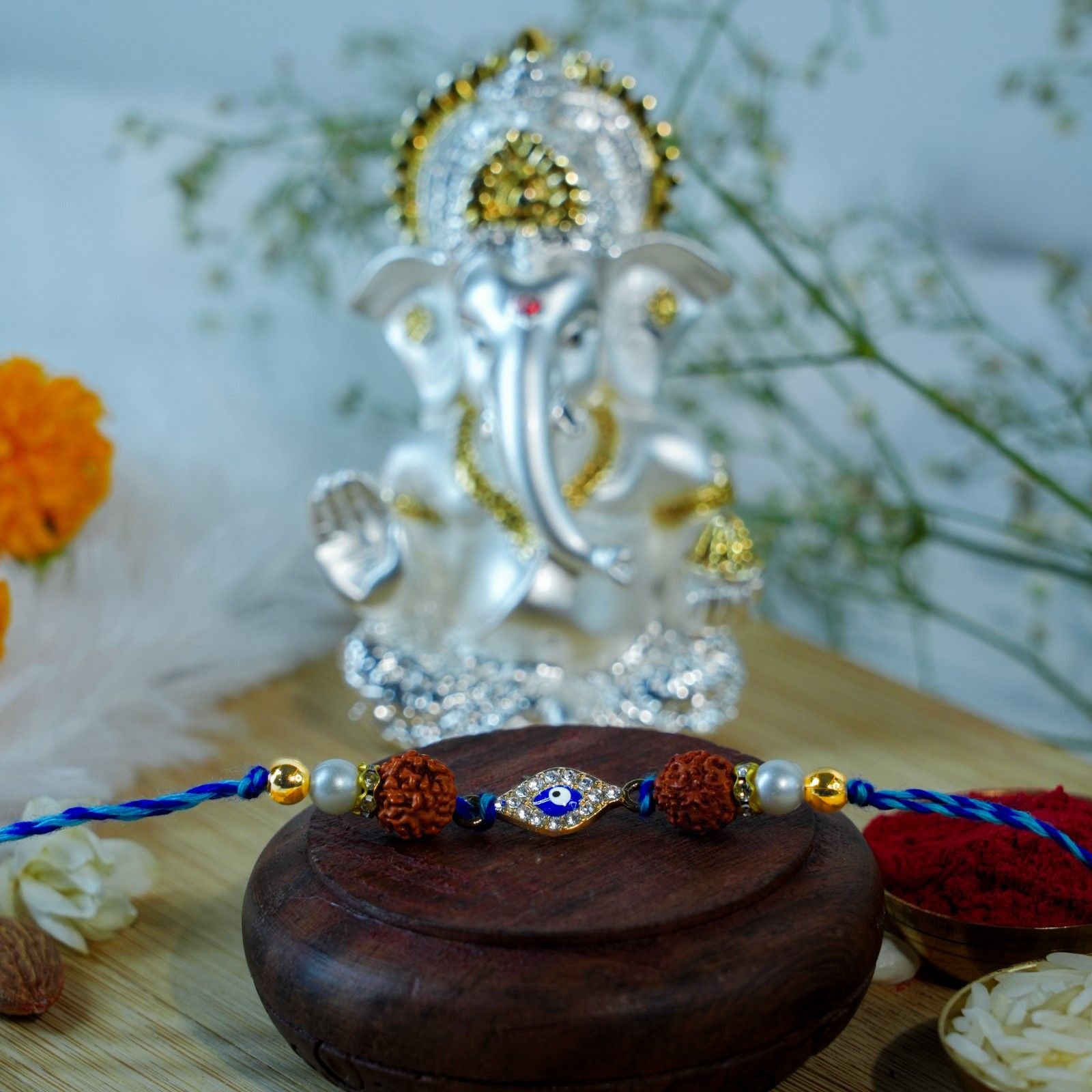Rudraksha and Evil Eye Rakhi placed before silver gold Ganesha idol for Raksha Bandhan.
